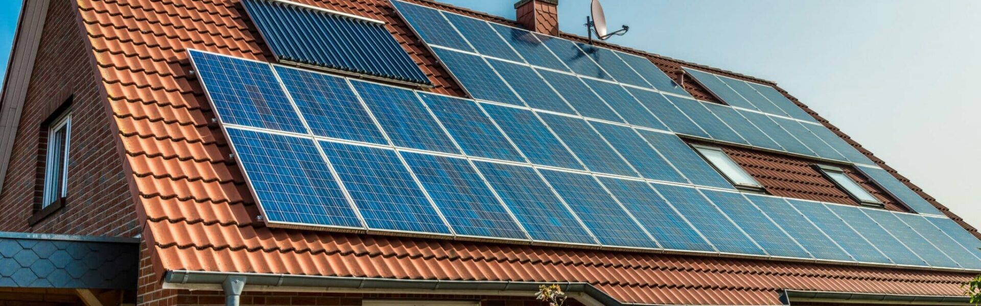 A closeup of a brick house with solar panels on its muted red roof