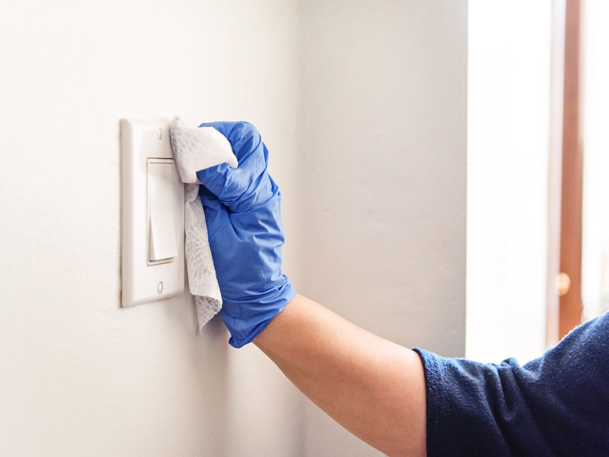 Cleaning a light switch with gloves and a damp cloth.